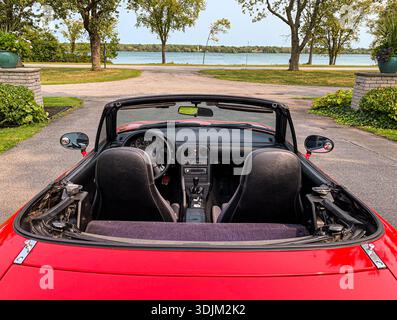 Bright red convertible with the top down reveals black leather seats and a polished dashboard. Open-air driving beside a lake creates a carefree, vaca Stock Photo