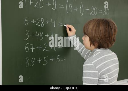Schoolboy doing math on chalkboard in classroom Stock Photo