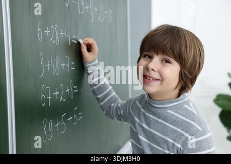 Schoolboy doing math on chalkboard in classroom Stock Photo