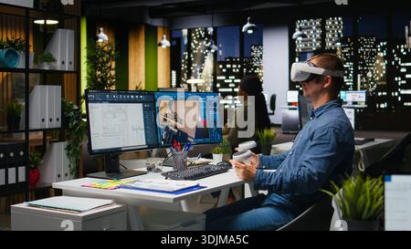 Interior designer using virtual reality headset to create a floor plan, working on apartment layout with architectural software and blueprints. VR glasses and CAD modeling program. Camera A. Stock Photo