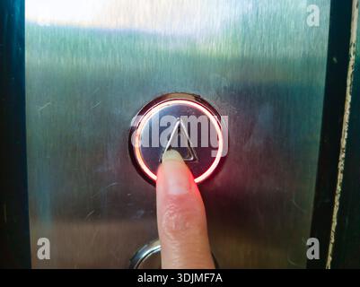 Close up of a finger pressing an illuminated red up arrow button inside an elevator at Ors vezer tere, Budapest. Concept of urban residential living, Stock Photo