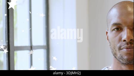 Facing camera, mid-adult man sitting by paned window wearing white top with white stars, copy space Stock Photo
