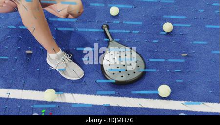 Squatting woman wearing gray sneakers and white socks on blue turf, with padel paddle and balls Stock Photo