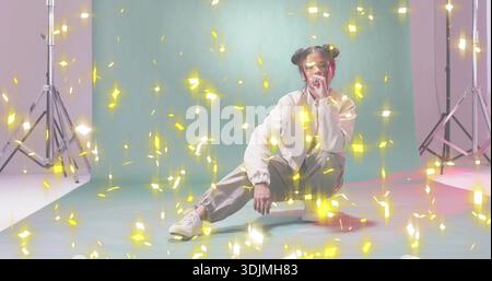 Posing female model crouching in studio on mint backdrop, wearing athletic wear, gold confetti Stock Photo
