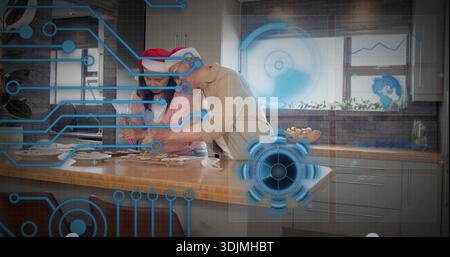 Preparing holiday cookies, woman and man wearing Santa hats at island in kitchen with blue AR Stock Photo