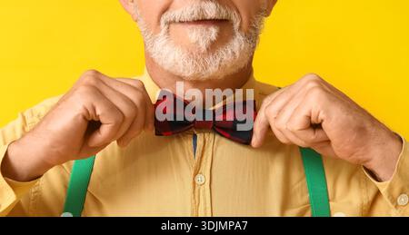 Handsome mature man adjusting bow tie on yellow background, closeup Stock Photo