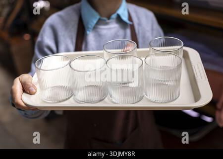 Waiter holding tray with four empty glass in cafe. Professional person at work providing customer service in restaurant, preparing to serve fresh drin Stock Photo