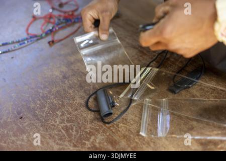 Person focused hands working, carefully assembling small electronic device. meticulous craft involving plastic bag, cable, and repair on wooden table Stock Photo