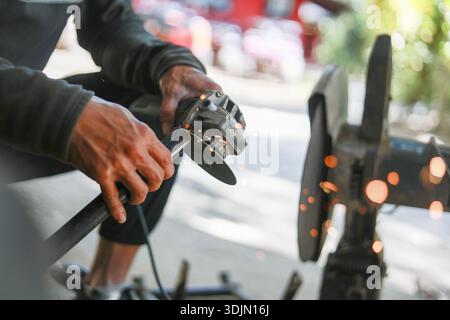 Focused craftsman grinding metal with power tool creating sparks. Close up of worker hands using an angle grinder showing skill and manual labor at wo Stock Photo