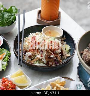 Asian-style salad with fresh herbs, vegetables, and spicy dressing served on a table with various accompaniments and condiments. Stock Photo