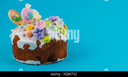 A round cake sits on a bright blue surface. The cake is topped with frosting, flowers, and Easter decorations like eggs and rabbits. It shows festive Stock Photo