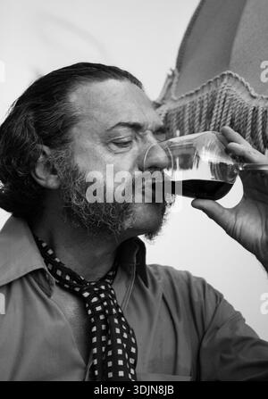 Vintage style monochrome photography of a sophisticated middle-aged man tasting wine, featuring a fringed sun umbrella in the background. Stock Photo