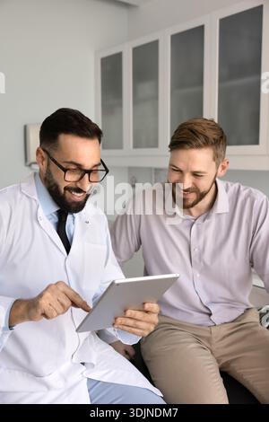 Happy doctor using tablet pc sharing good news with patient Stock Photo