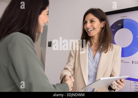 Two multiethnic businesswomen shaking hands standing in modern office Stock Photo
