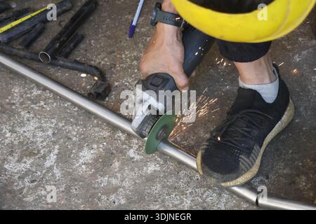 Focused worker in workshop using an angle grinder to cut metal pipe, creating bright sparks. industrial process requires safety and precision for job Stock Photo