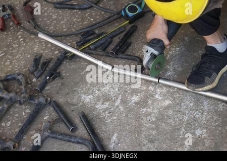 Focused industrial worker wearing safety helmet cutting metal pipe. construction job involves grinding with power tool on concrete floor for fabricati Stock Photo