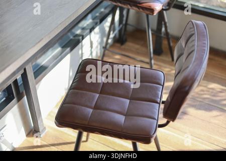 Comfortable brown leather bar stool chair in modern vintage interior. This inviting furniture offers moment of relaxation by window with warm natural Stock Photo