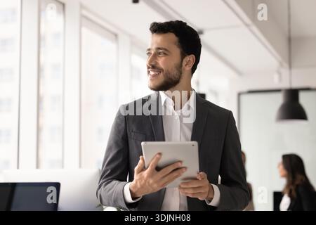 Happy businessman in elegant formal suit holding digital tablet indoors Stock Photo