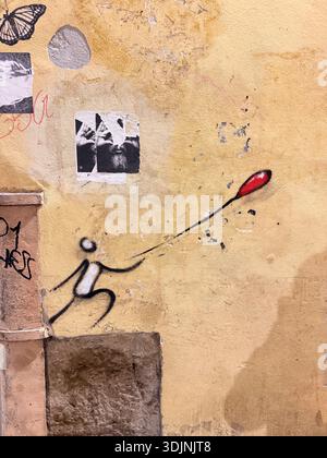 A textured, weathered yellow wall in Florence features urban art. Stock Photo