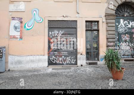 Graffiti-covered shutters and walls in Rome, Italy. The facade is a mix of pastel yellow and gray stone. Stock Photo
