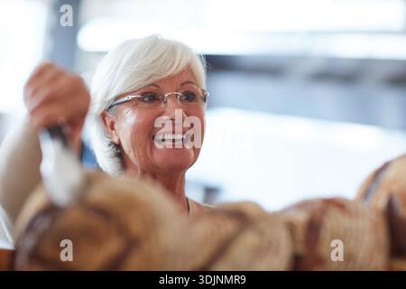 Happy, serving and senior woman in bakery with order, bread selection or customer service in store. Smile, hospitality and elderly female owner or Stock Photo