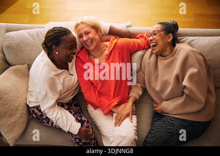 High angle view of carefree multiracial female friends laughing with each other while sitting on sofa at home Stock Photo