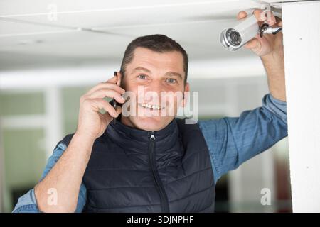 smiling contractor by cctv camera using smartphone Stock Photo