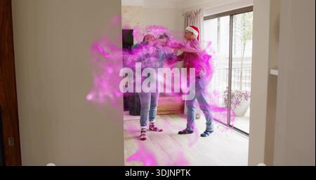Standing couple in casual clothes reaching amid pink smoke in living room, Santa hat visible Stock Photo