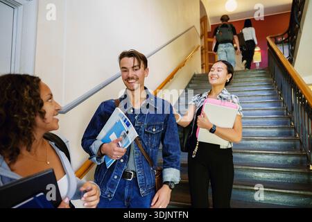 Portrait of smiling young man enjoying leisure time with female friends near staircase in university campus Stock Photo