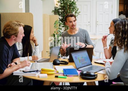 Young man discussing ideas with friends sitting at table for group project in university campus Stock Photo