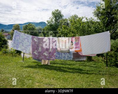 Various blankets and colorful bed sheets hanging on a long clothesline in an outdoor grassy garden Stock Photo