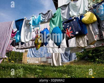 Various clothes, colorful pillows, and a large blue bag with the Australian flag hanging on a clothesline in a sunny outdoor garden Stock Photo