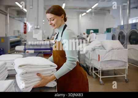 A woman worker in an apron holds fresh towels in a laundromat Stock Photo