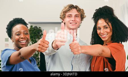 Three Friends Give Thumbs Up in Modern Office, Celebrating Teamwork and Success Stock Photo