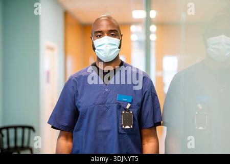 Portrait of bald male doctor wearing face mask standing in hospital corridor Stock Photo