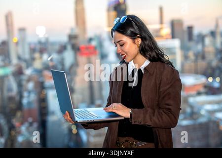 Young businesswoman using laptop on new york rooftop Stock Photo