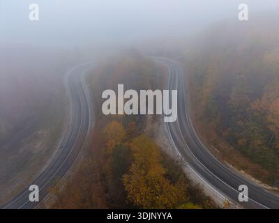 Aerial view of foggy winding road through autumn forest landscape Stock Photo