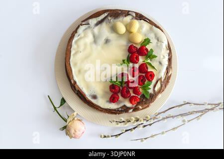 Festive Easter greeting with raspberry cake, floral elements, willow branch arranged on white. Stock Photo