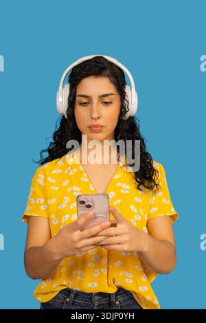 Young woman listening to music on her phone, wearing white headphones and a yellow shirt Stock Photo