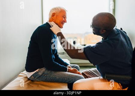 Male medical professional checking throat of senior man in examination room at hospital Stock Photo
