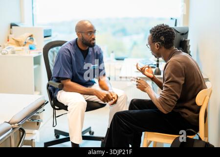 Young man communicating through sign language with male doctor while sitting in hospital room Stock Photo