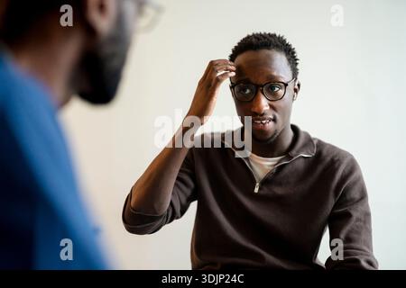 Young man with hearing problem using sign language while communicating with doctor in clinic Stock Photo