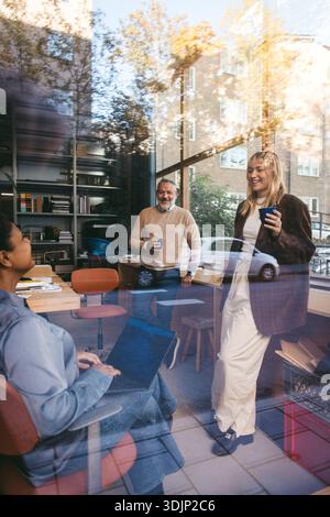 Female manager talking with colleagues during meeting in office seen from glass Stock Photo