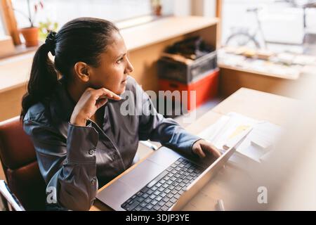 High angle view of thoughtful female business expert looking away while sitting with laptop in design office Stock Photo