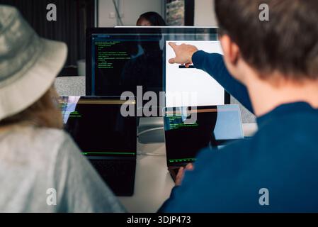 Rear view of male and female programmers discussing with each other on desktop PC in office Stock Photo