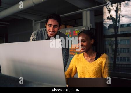 Smiling female programmer using computer while sitting beside male colleague in tech office Stock Photo