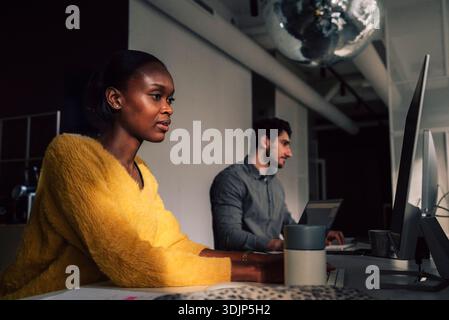 Focused female tech expert working on desktop PC while sitting with male colleague in startup office Stock Photo