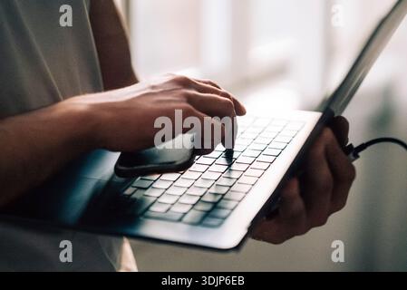 Hand of businessman holding smart phone while pressing laptop key Stock Photo