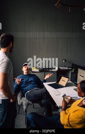 High angle view of male entrepreneur discussing with colleagues while sitting at desk in tech office Stock Photo