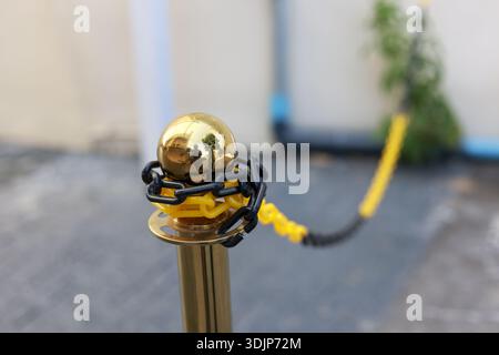 Close up of golden stanchion barrier pole with yellow rope. shiny, reflective metal ball top and black chain detail suggest an exclusive entrance or c Stock Photo